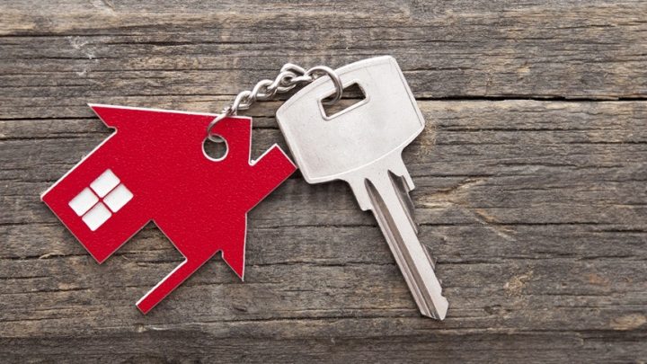 Ein Schlüssel mit einem roten Haus als Schlüsselanhänger liegt auf einem Holztisch.