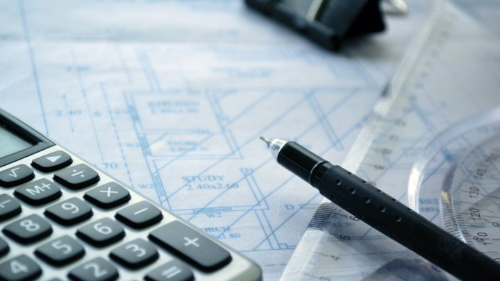 Das Bild zeigt eine Bauzeichnung, Stift und Tascehnrechner zur Kalkulation von Baukosten