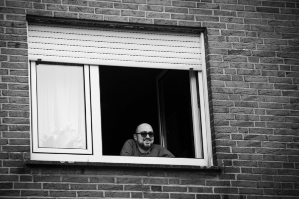 Das Foto zeigt das Fenster eines Wohnhauses, aus dem ein Mann herausschaut. Der Mann heißt Mesut Can, lebt in Bielefeld und berichtet in einem Podcast über sein Quartier